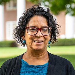 Lady with dark curly hair wearing glasses, black cardigan and blue top