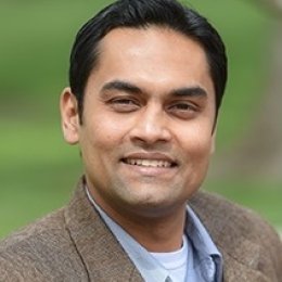 Man with dark hair wearing sports coat with blue button up dress shirt