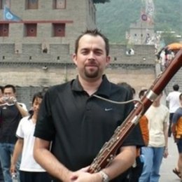 Man wearing black nike polo holding basson in front of historic building abroad