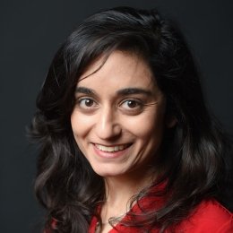 Lady with dark curly hair wearing red top in front of black background