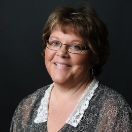 lady with short brunette hair and glasses with black and white top in front of black background