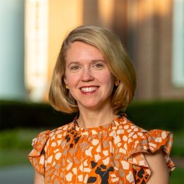 Lady with short blonde hair wearing multi colored orange and gold top