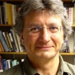 Man with short grey hair wearing glasses standing in front of library