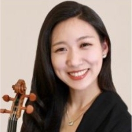 Lady with dark hair and black top holding violin and smiling