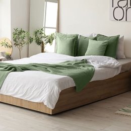 A double bed with green and white covering and pillows in a white room