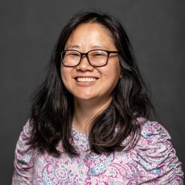 Jessica Leonard headshot - lady wearing glasses and pink paisley top in front of grey background