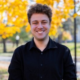 Eric Matherly headshot man with brown hair in black sweater standing in front of yellow tree in fall