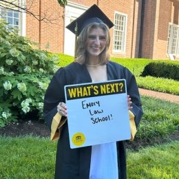 Student in cap &amp; gown holding a whiteboard with emory law school in text