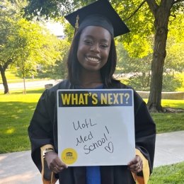 Student in cap &amp; gown holding a whiteboard with U of L med school text
