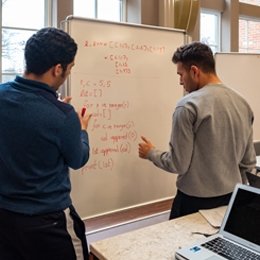 Two students standing at white board working out Math problems