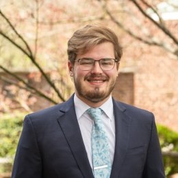 Student wearing suit and glasses and smiling at camera