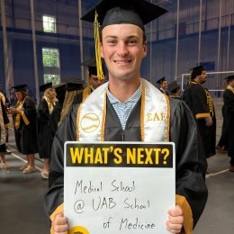 A graduate holds a sign noting "What's Next? Med School at UAB School of Medicine"