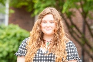 student with long hair wearing black and khaki gingham dress