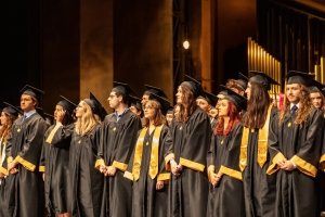 Large group of students standing facing crowd in cap and gown at graduation ceremony