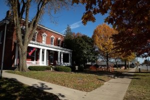 A two-story brick building with white columns is fronted by a small lawn and a sidewalk
