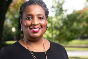 A woman smiles for a portrait in front of a background of trees.