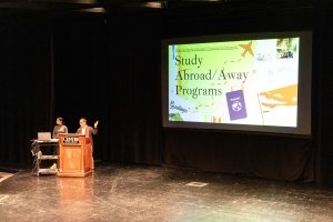 Two people stand behind a podium while a projection screen introduces Centre College Study Abroad & Away programs.