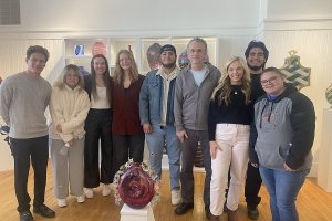 Students pose for a photo behind their contributed piece to the GLASS National Art Museum.