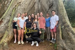 CentreTerm students in Ghana - group of students standing in front of large tree roots. One student holding Centre pennant.