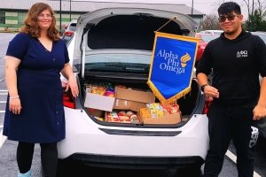 Students standing at car with open trunk showing collected food from APO food drive to benefit the New Hope Food Pantry