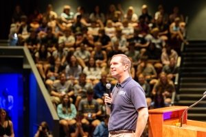 A man with a microphone talks to an audience.