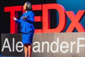 A woman speaks from a stage with the words TED x behind her.