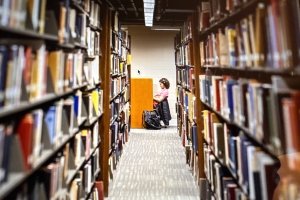 inside Grace Doherty Library with stacks of books on each side of row and student studying at end of row
