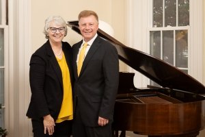 A woman and a man pose together next to a piano.