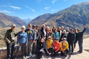 A large group poses for a photo on an overlook with rugged mountains and a valley behind them.