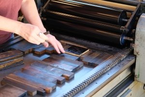 Two hands place panels on an old-fashioned letterpress printing press.