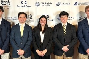 Two young men stand on either side of a young woman, all waring business suits and posing for a photo together.