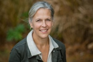 A woman wearing a collared shirt and a jacket poses for a photo outdoors.