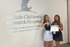 Two Tri-Delta leaders are standing in front of a St. Jude sign holding their philanthropy award.