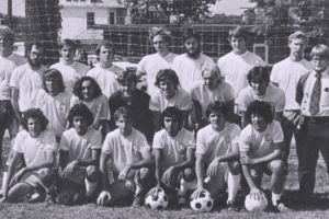 A black-and-white photo shows a soccer team posing for a photo with one row kneeling in the front and others standing behind them.