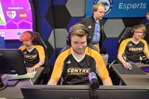 A man in a black and gold Centre College jersey if flanked by two teammates as he competes in an Esports tournament.