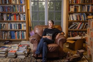 Centre College Professor of English Stacey Peebles sits in a leather armchair in a room filled with loaded book shelves and piles of books on the floor, the personal library of American author Cormac McCarthy.