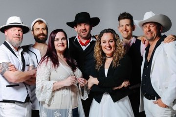 The seven members of The Seven Wonders pose against a gray backdrop, all smile at the camera