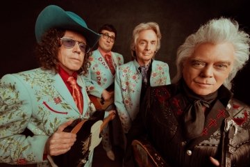 Marty Stuart and his band members pose against a black background with a wide distorted angle
