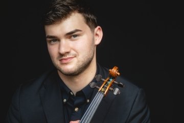 Nathan Metlzer headshot against a black background, with his violin resting against his shoulder