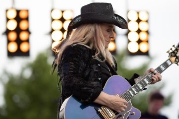 Melissa Etheridge performing a show, playing guitar with a cowboy hat on