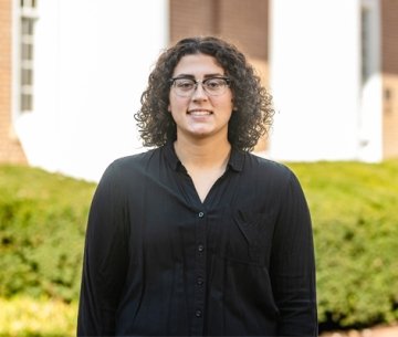 Student wearing dark shirt and glasses and smiling