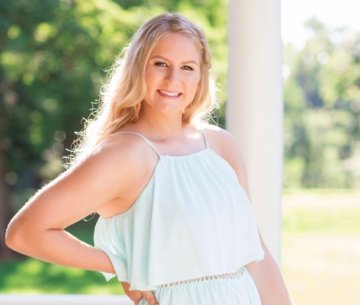Student wearing dress standing on porch smiling with hand on hip
