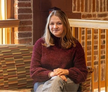 Student sitting down with hands folded on lap and smiling at camera