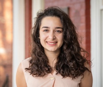 Student with long brown hair standing on porch and smiling at camera