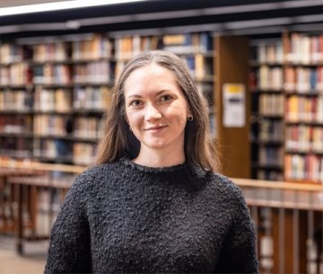 Person standing inside library and smiling at photographer