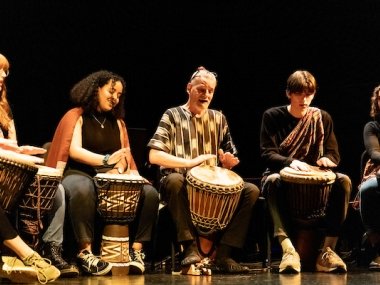 Students and the ensemble director play drums as part of a performance by the African Drum Ensemble.