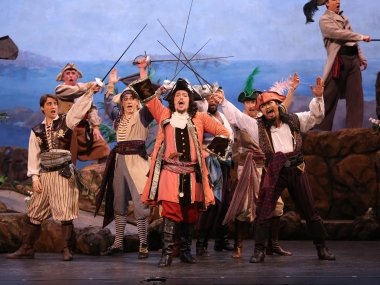 Performers dressed as pirates on stage, holding swords in the air