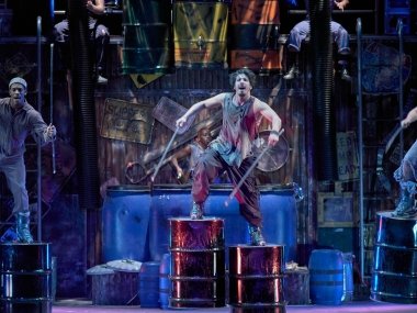 Three men dancing while standing on barrels strapped to their feet.