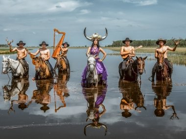 5 men and one woman each riding a horse. The horses are standing in water up to their chests.