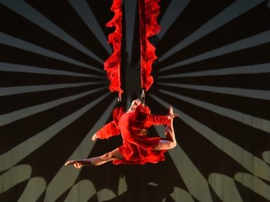 A dancer suspended in the air by 2 red ropes